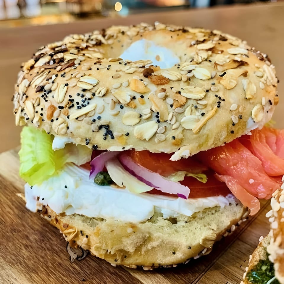 Close-up of a bagel with cream cheese, smoked salmon, lettuce, tomato, red onion, and capers.