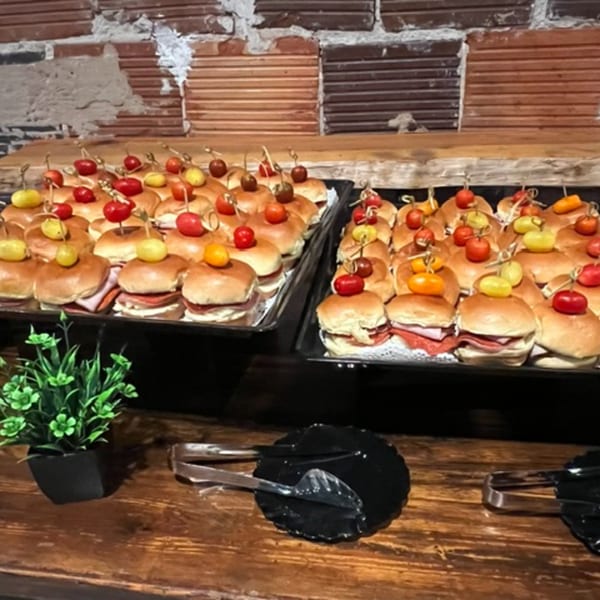 Trays of mini sandwiches with cherry tomato and olive skewers on a wooden table.
