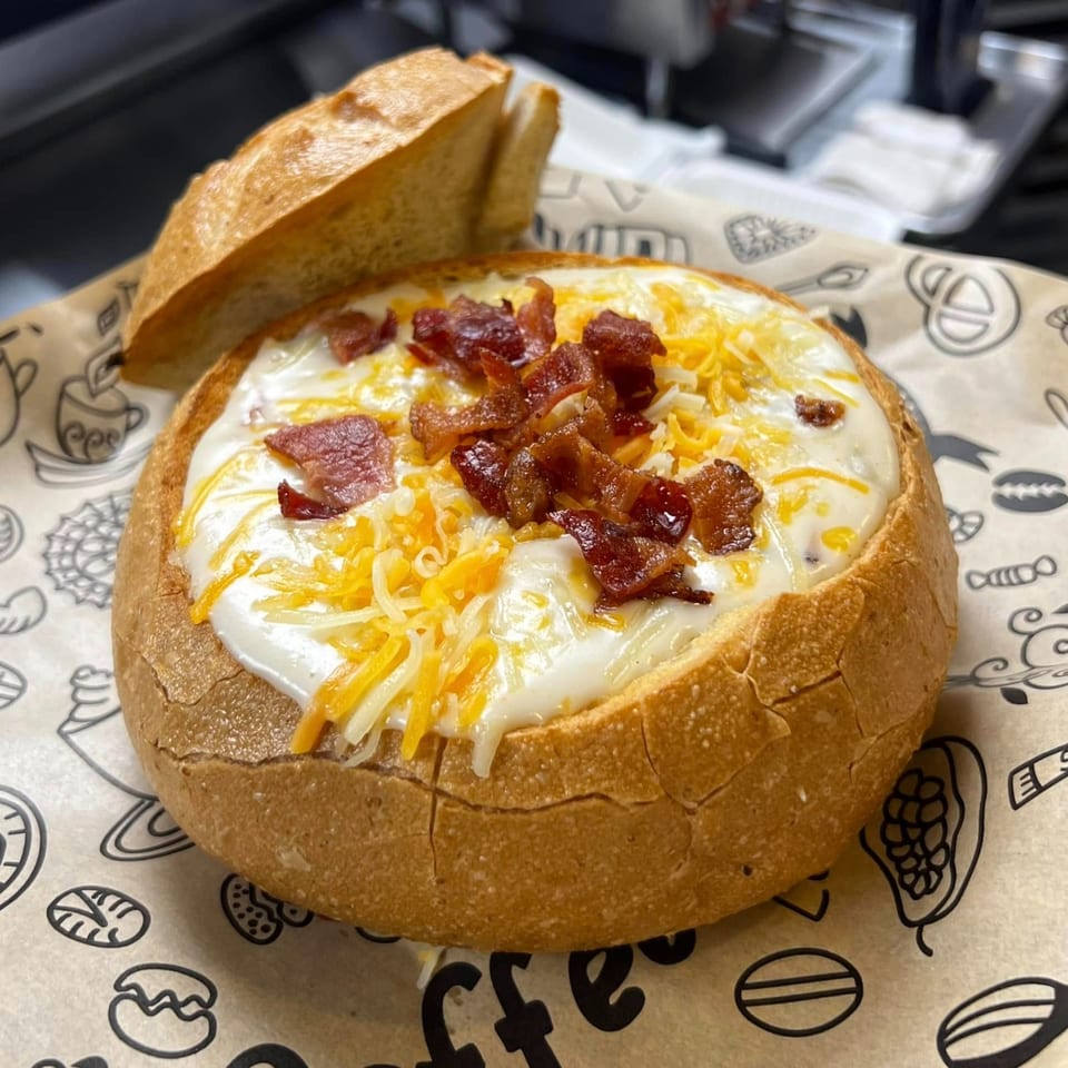 Creamy soup in a bread bowl, topped with shredded cheese and crispy bacon bits, served at Mary's Bagel Café.