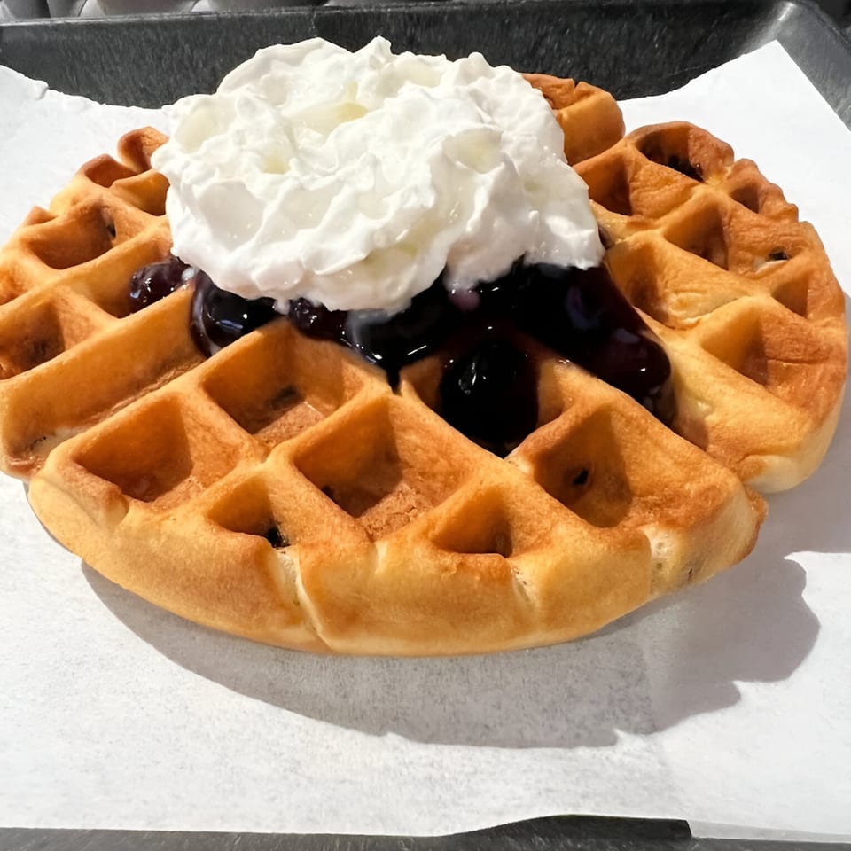 Golden waffle topped with dark berry compote and a generous dollop of whipped cream.