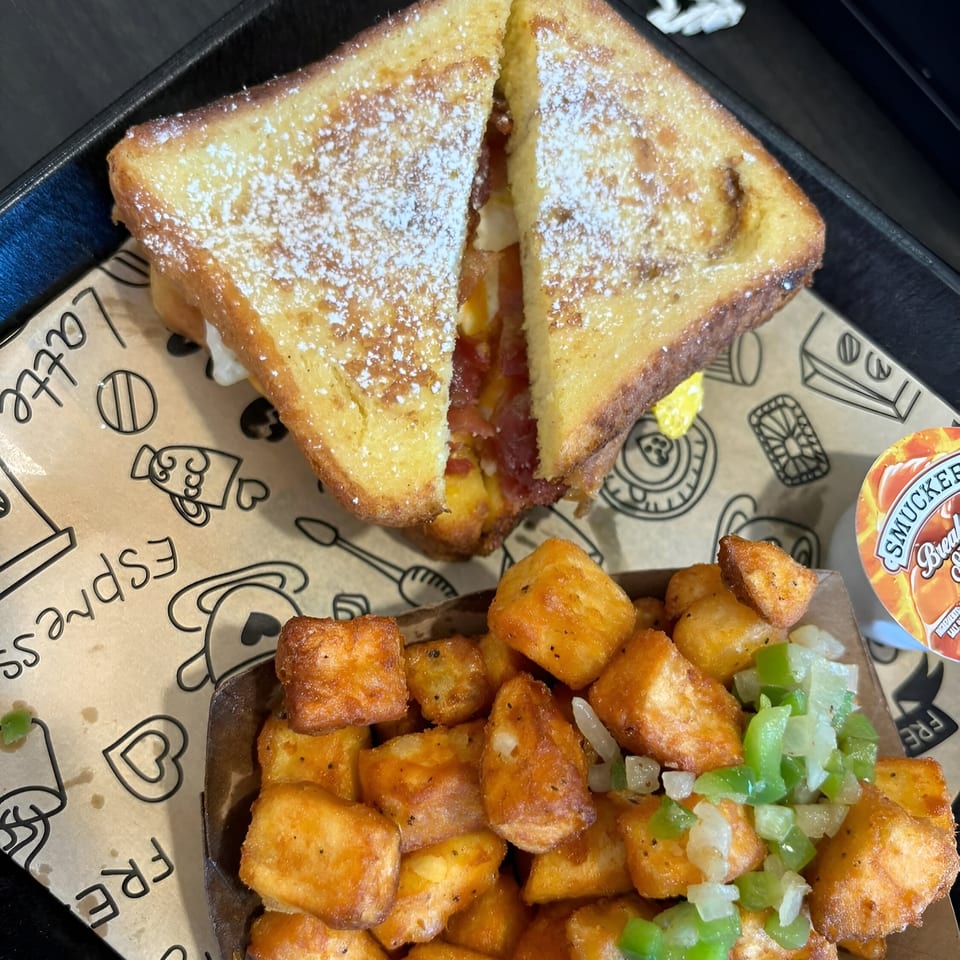 French toast sandwich with powdered sugar, bacon, and egg, served with crispy home fries.