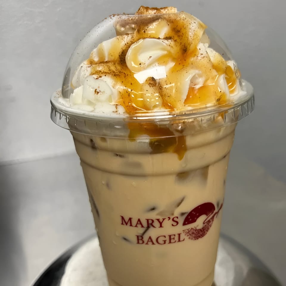 Iced coffee with whipped cream, caramel drizzle, and cinnamon in a Mary's Bagel branded cup.