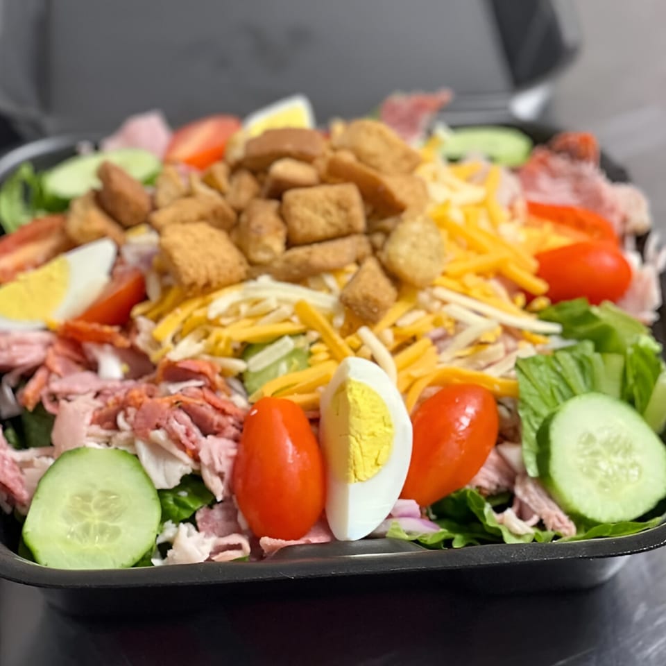 A vibrant chef salad with ham, cheese, croutons, tomatoes, cucumbers, and hard-boiled eggs.