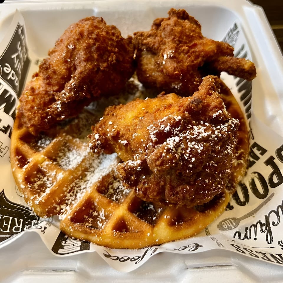 Crispy fried chicken pieces and a waffle dusted with powdered sugar in a takeout container.